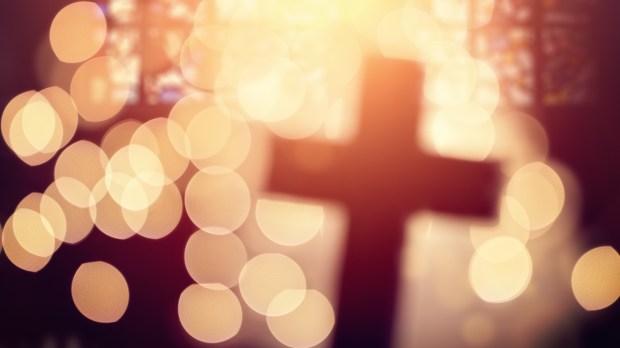 Abstract defocussed cross silhouette in church interior against stained glass window concept for religion and prayer