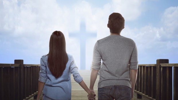 couple standing holding hands in front of cross