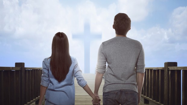 couple standing holding hands in front of cross