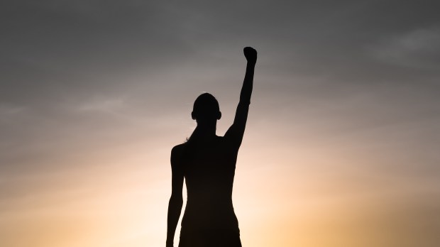 Strong, victorious , and motivated young woman raising her fist up to the sunset sky