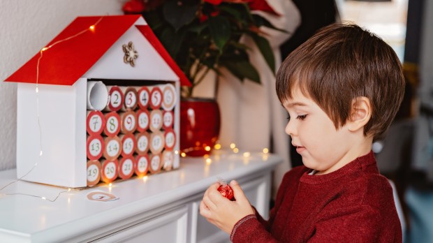 Little child taking chocolate opening first day in handmade advent calendar made from toilet paper rolls