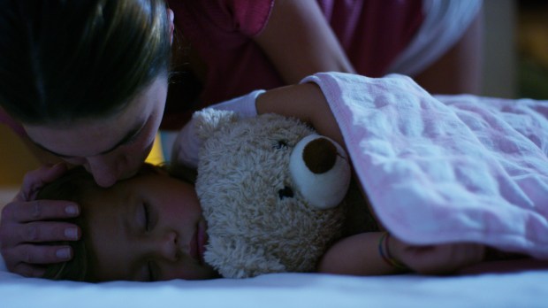 mother tucking in child with teddy bear