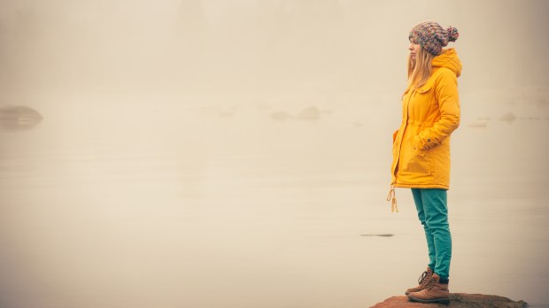 young woman facing water outside on rock