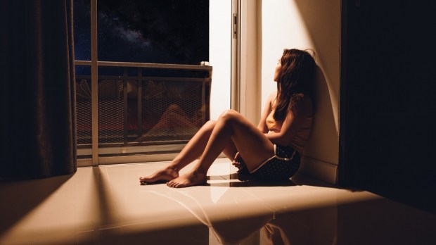 Sad woman sitting on floor looking out window