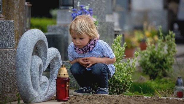 Little-toddler-boy-sitting-on-a-grave-in-cemetery-sad-and-lonely-shutterstock
