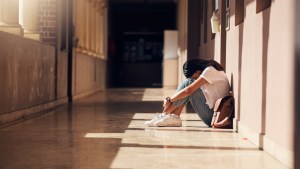 pogrążona w smutku młoda dziewczyna z liceum siedzi samotnie na szkolnym korytarzu i chowa głowę
