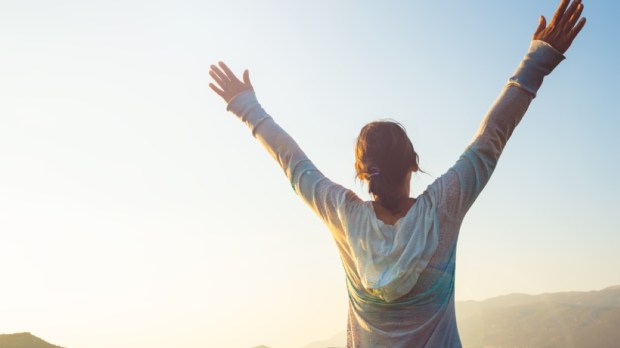 Happy traveler, woman with open arms stands on the rock