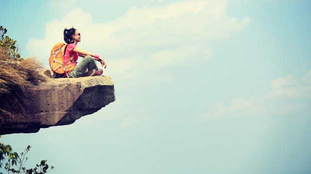 backpacker on rocky cliff looking out at sky