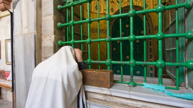 A jewish man is praying in front of the tomb of patriarch Abraham.