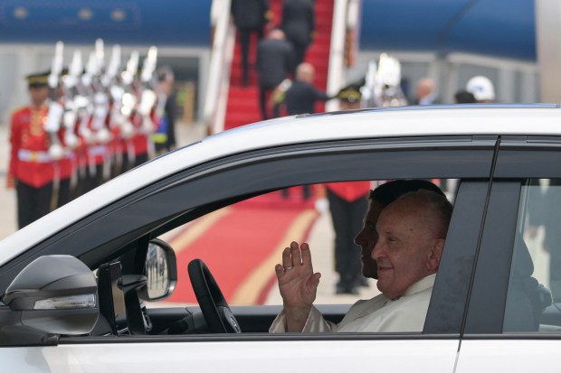 Pope Francis waves from a departing vehicle following his arrival at Soekarno-Hatta International Airport in Jakarta on September 3, 2024